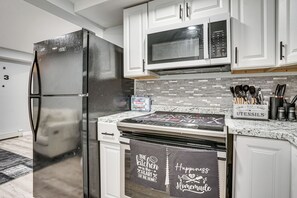 A kitchen with white cabinets, a stainless steel refrigerator, a microwave, and a stove. There are kitchen utensils and a First Aid kit visible.