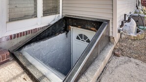A narrow, enclosed space with a door, a window with blinds, and a small step leading up to it.