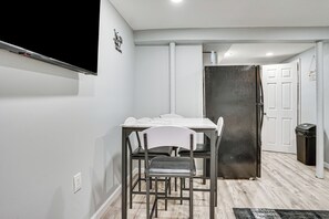 A modern kitchen with a white table, black chairs, a stainless steel refrigerator, and a white door.