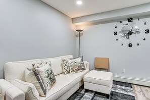 A modern living room with a sofa, ottoman, and a wall clock.