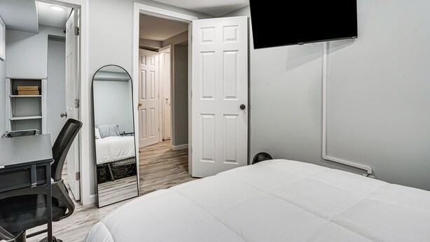 A bedroom with a bed, a desk, a chair, a TV, and a mirror.