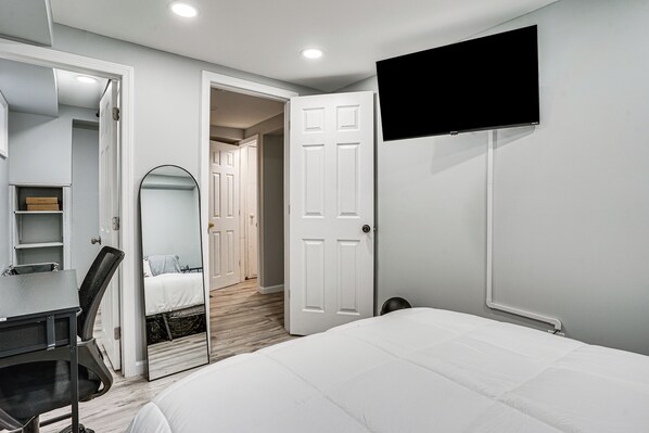 Un dormitorio con cama, escritorio, silla, televisor y espejo.