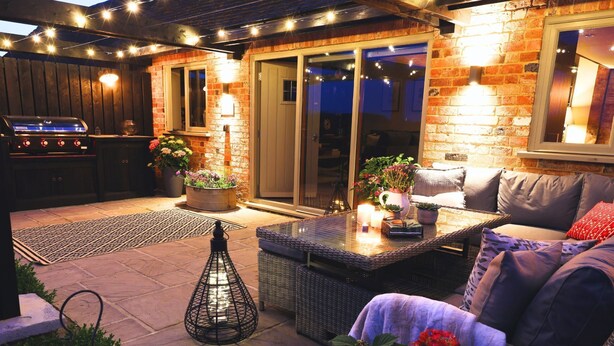 Een terras buiten met een barbecue, zithoek en potplanten.