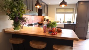 Een keuken met een houten kookeiland, barkrukken, een potplant, een fles champagne en een schaal tomaten.