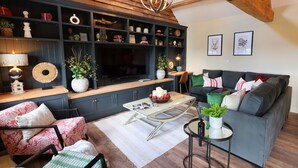 Een woonkamer met een donkerblauwe tv-kast, een houten plafond, een grijze bank en een ronde salontafel.