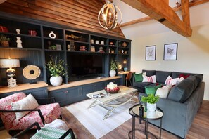 Ein Wohnzimmer mit einer dunkelblauen Unterhaltungsanlage, einer Holzbalkendecke, einem grauen Sofa und einem runden Couchtisch.