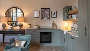 Cucina con piano cottura, forno e lavello, una sedia e quadri appesi al muro.