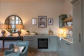 Een keuken met een fornuis, oven en spoelbak, een stoel en ingelijste foto’s aan de muur.