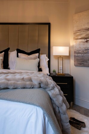 Een slaapkamer met een groot bed, een nachtkastje met een lamp en een aan de muur hangend kunstwerk.