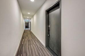 A hallway with a carpeted floor, a door on the right, and a light fixture on the ceiling.