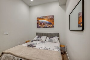A bedroom with a bed, pillows, a nightstand, a wall-mounted mirror, and a painting. - Long-Term Stay in Denver! Dog-Friendly Studio (Denver)