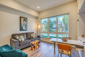 A modern living room with a sofa, a dining table, and a large window with a view of houses.