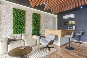 Ein stilvoller Lounge-Bereich mit Backsteinwand, vertikalen Grünflächen, einem Ledersofa, einem runden Couchtisch und einem Holzbüro.