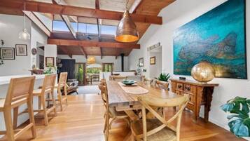 A spacious dining area with wooden furniture, a large painting, and a high ceiling with exposed beams.