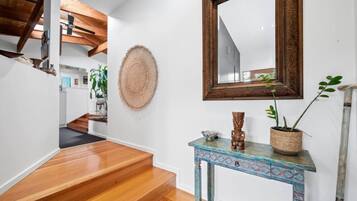 A staircase with wooden steps leading to a landing, a round woven wall hanging, a mirror with an ornate frame, and a small table with a plant and decorative items.