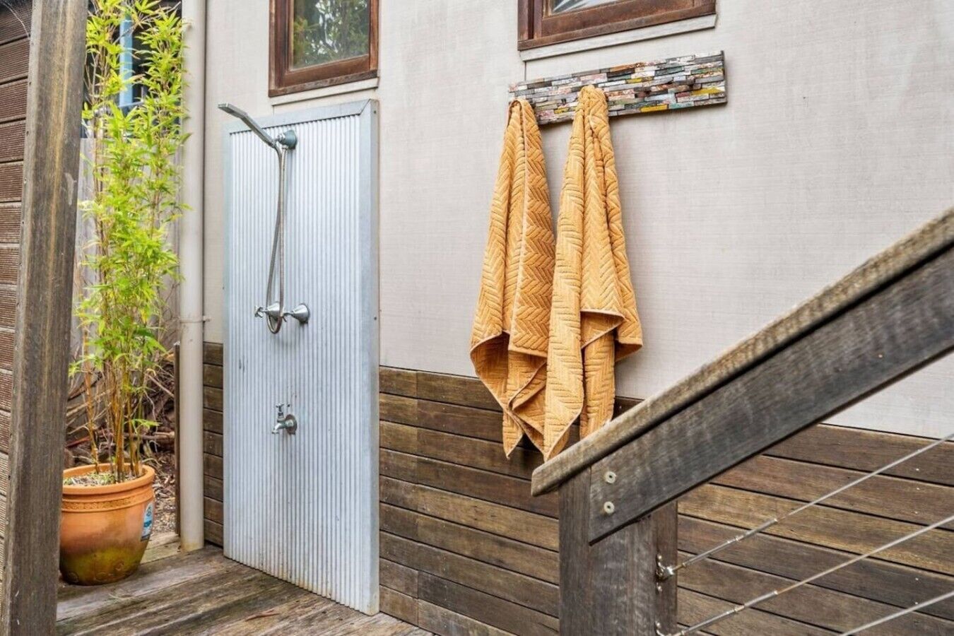A wooden staircase with a metal railing, a potted plant, a door with a shower, and towels hanging on a rack.