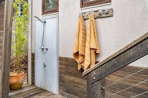 Eine Holztreppe mit Metallgeländer, ein Blumentopf, eine Tür mit Dusche und Handtücher an einem Wäscheständer.