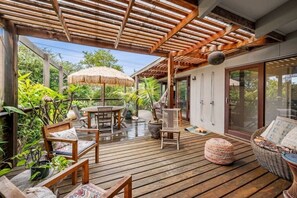 Eine Holzterrasse mit Gartenmöbeln, einem Strohdachschirm und Kübelpflanzen.