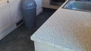 A kitchen with light wooden cabinets, a gas stove, an oven, a trash bin, and a granite countertop.