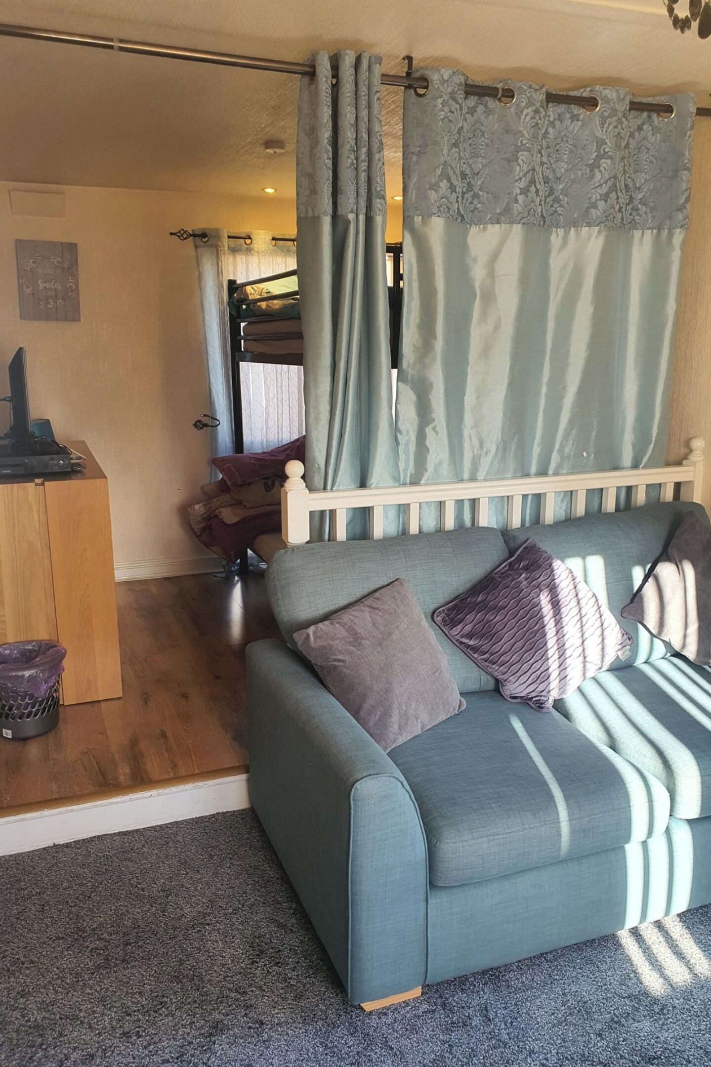 A room with a grey sofa, a wooden desk, a grey carpet, and a curtain with a floral pattern.
