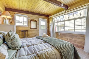 Un dormitorio de cabaña de madera con cama, lámpara, espejo y ventana.