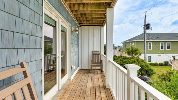 Une terrasse en bois avec une balustrade blanche, une chaise en bois et une porte donnant sur un porche.