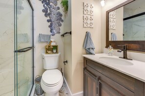 Ein Badezimmer mit Duschkabine aus Glas, Toilette, Waschbecken mit Spiegel, Wandbildern und einem Handtuchhalter.