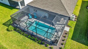 Ein Schwimmbad mit Glasüberdachung, umgeben von einer gepflegten Rasenfläche und einem Haus im Hintergrund.