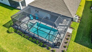 A swimming pool with a glass enclosure, surrounded by a well-maintained lawn and a house in the background. - Resort Golf Living: New Home, Elite Club Perks (Lehigh Acres)