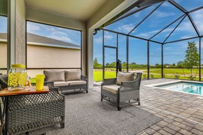 A covered patio with wicker furniture, a pool, and a view of a golf course. - Resort Golf Living: New Home, Elite Club Perks (Lehigh Acres)