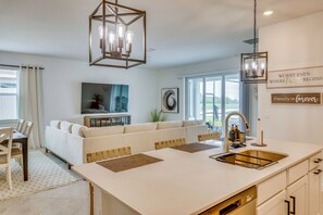 A modern kitchen with a central island, pendant lighting, and a dining area with a sofa and chairs. - Resort Golf Living: New Home, Elite Club Perks (Lehigh Acres)