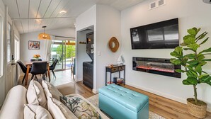 Una sala de estar moderna con un sofá, un otoman azul, una chimenea y un comedor con una mesa y sillas.