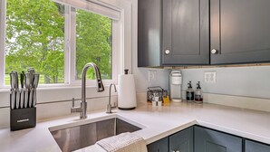 Una cocina moderna con un lavamanos de acero inoxidable, una ventana con vistas a árboles y armarios oscuros.