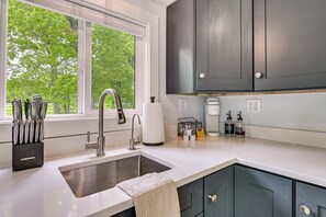 A modern kitchen with a stainless steel sink, a window with a view of trees, and dark cabinets.