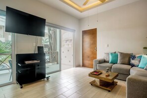 A modern living room with a flat-screen TV, a sofa, a coffee table, and a sliding glass door leading to a balcony. - Modern Condo: Steps to Mamitas Beach Club/5thAve (Playa del Carmen)