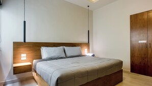 Una camera da letto moderna con una testiera in legno, un letto con copriletto grigio, abat-jour e un armadio.