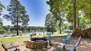 A lakeside outdoor seating area with a stone fire pit, picnic tables, and Adirondack chairs. - It's Our Pleasure! Lake Escape w/ Boat Ramp (Macon)