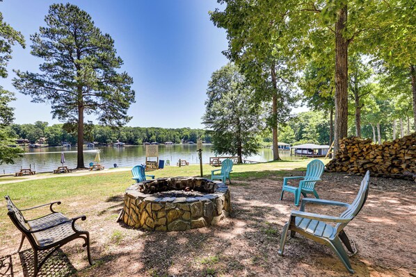 Un espace extérieur aménagé au bord du lac, avec un foyer en pierre, des tables de pique-nique et des fauteuils Adirondack.