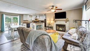 A spacious living area with a sofa, a coffee table, and a fireplace. There is a kitchen in the background with a dining area. - It's Our Pleasure! Lake Escape w/ Boat Ramp (Macon)