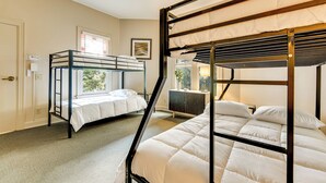 Een kamer met stapelbedden, een raam met zonwering, een bureau en een kast.
