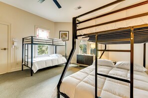A room with bunk beds, a window with blinds, a desk, and a cabinet.