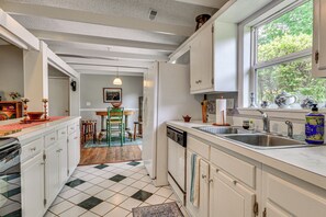 Cucina con mobili bianchi, lavastoviglie, lavello e finestra vista alberi.
