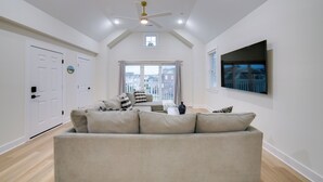 Un salon spacieux avec un plafond haut, un ventilateur de plafond, une grande fenêtre offrant une belle vue, un téléviseur à écran plat fixé au mur et un canapé beige.