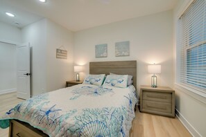 A bedroom with a bed, two bedside tables with lamps, a wooden headboard, and a window with blinds.