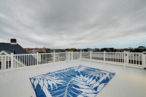 En tagterrasse med et hvidt hegn, en blå stribet måtte og udsigt til huse i baggrunden.