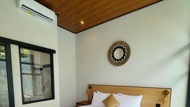 Una habitación de hotel con techo de madera, una cama con ropa de cama blanca y dorada, una toalla sobre la cama, una mesita de noche y un espejo montado en la pared.