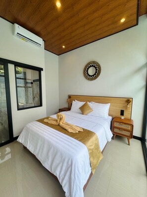 Une chambre d’hôtel avec un plafond en bois, un lit avec une literie blanche et dorée, une serviette sur le lit, une table de chevet et un miroir fixé au mur.