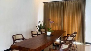 Una sala de conferencias con una larga mesa, seis sillas, una planta en maceta y una cortina.
