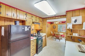 A kitchen with wooden cabinets, a refrigerator, an oven, a dining table with chairs, and a window with a view of greenery. - Year-Round Mtn Escape in the 'Arizona Rockies' (Lakeside)