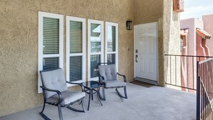 A balcony with three rocking chairs and a glass table, a white door, and a textured wall. - Grand Prix Energy 1 Mi From the Strip (Las Vegas)
